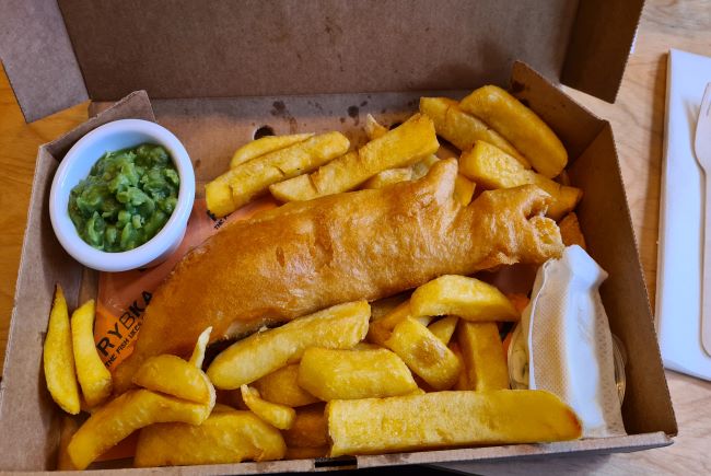 Image shows fish, chips and peas in a cardboard takeaway box. 